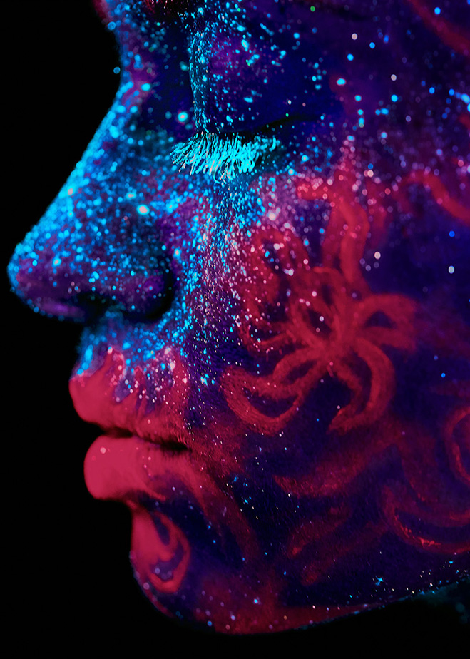 Side headshot of female painted in blue and crimson ultraviolet.