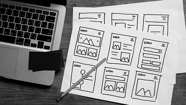 Ariel shot of open laptop on left with sketches of website page layouts on right.